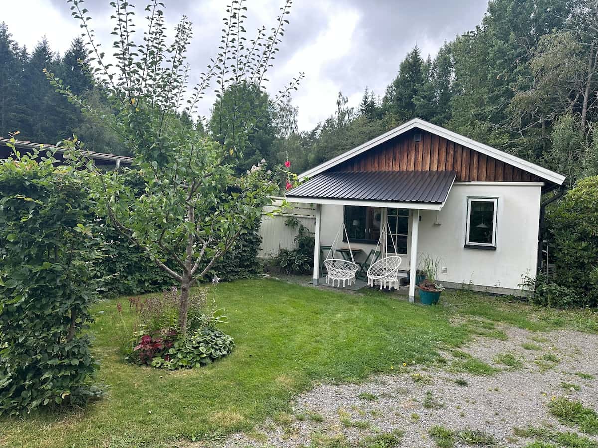 Vita huset i trädgården med äppleträd och hängande stolar.